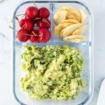 Avocado Eier Salat in einer Lunchbox mit Crackern und Kirschen, Scheibtisch-Gegenst&auml;nde liegen im Bildrand.