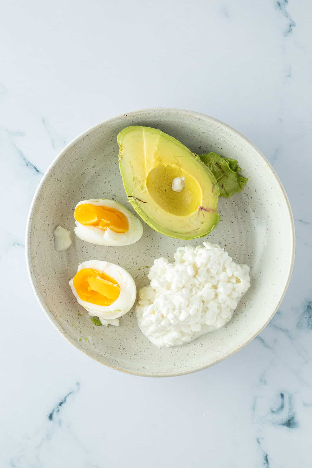 Gekochtes Ei, eine halbe Avocado und etwas H&uuml;ttenk&auml;se in einem Teller.