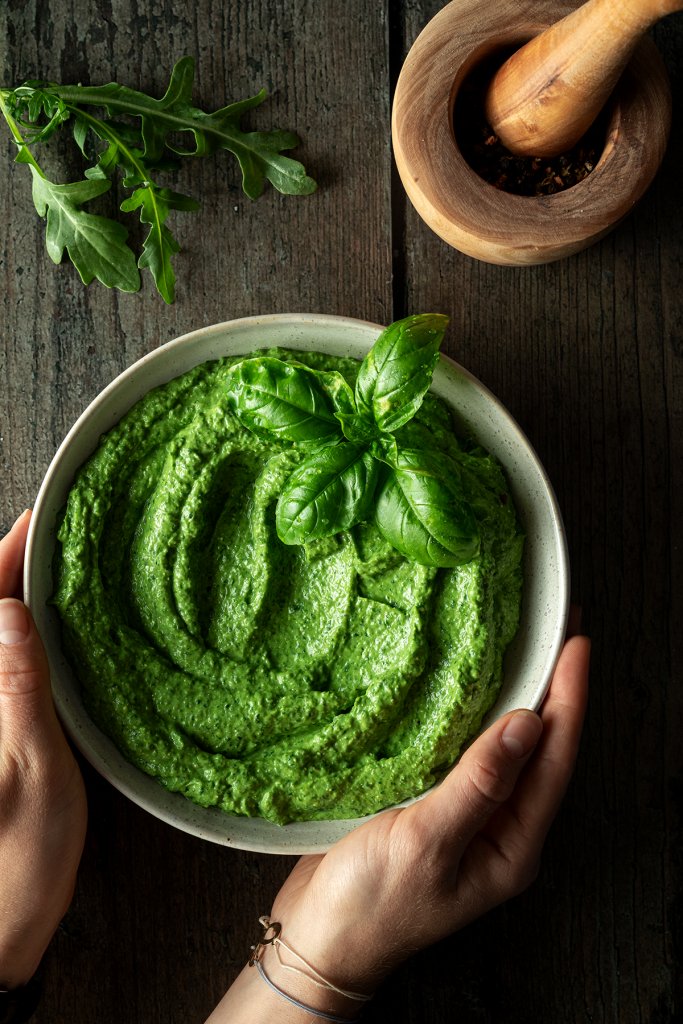 Cremige Avocado Pesto in einer Sch&uuml;ssel, die mit den H&auml;nden auf ein Holztisch gestellt wird.