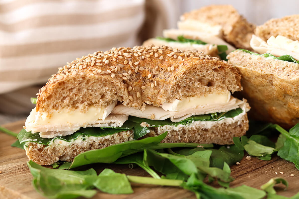 Halbiertes Bagel Sandwich belegt mit K&auml;se, Salat und Schinken.