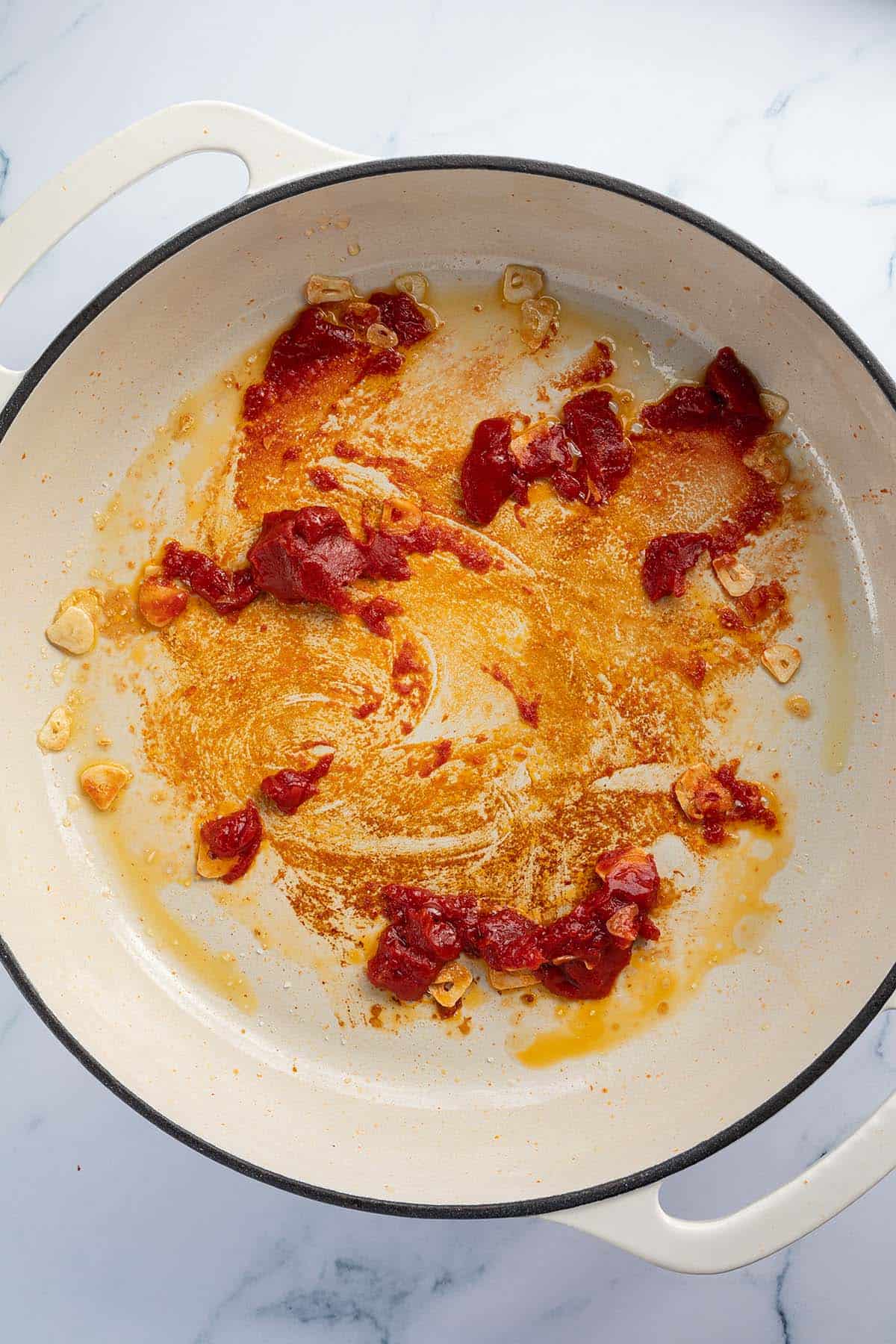 Knoblauch, Sirup und Tomatenmark werden in einer Pfanne angebraten.