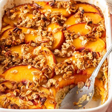 Baked Oatmeal in Auflaufform mit Pfirsich Spalten und Haferflocken Streusel on top. Ein L&ouml;ffel hat eine Portion herausgenommen.