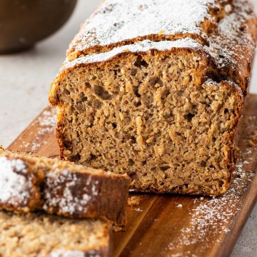 Bananenbrot mit Haferflocken und Puderzucker serviert mit einer Sch&uuml;ssel Beeren im Hintergrund.