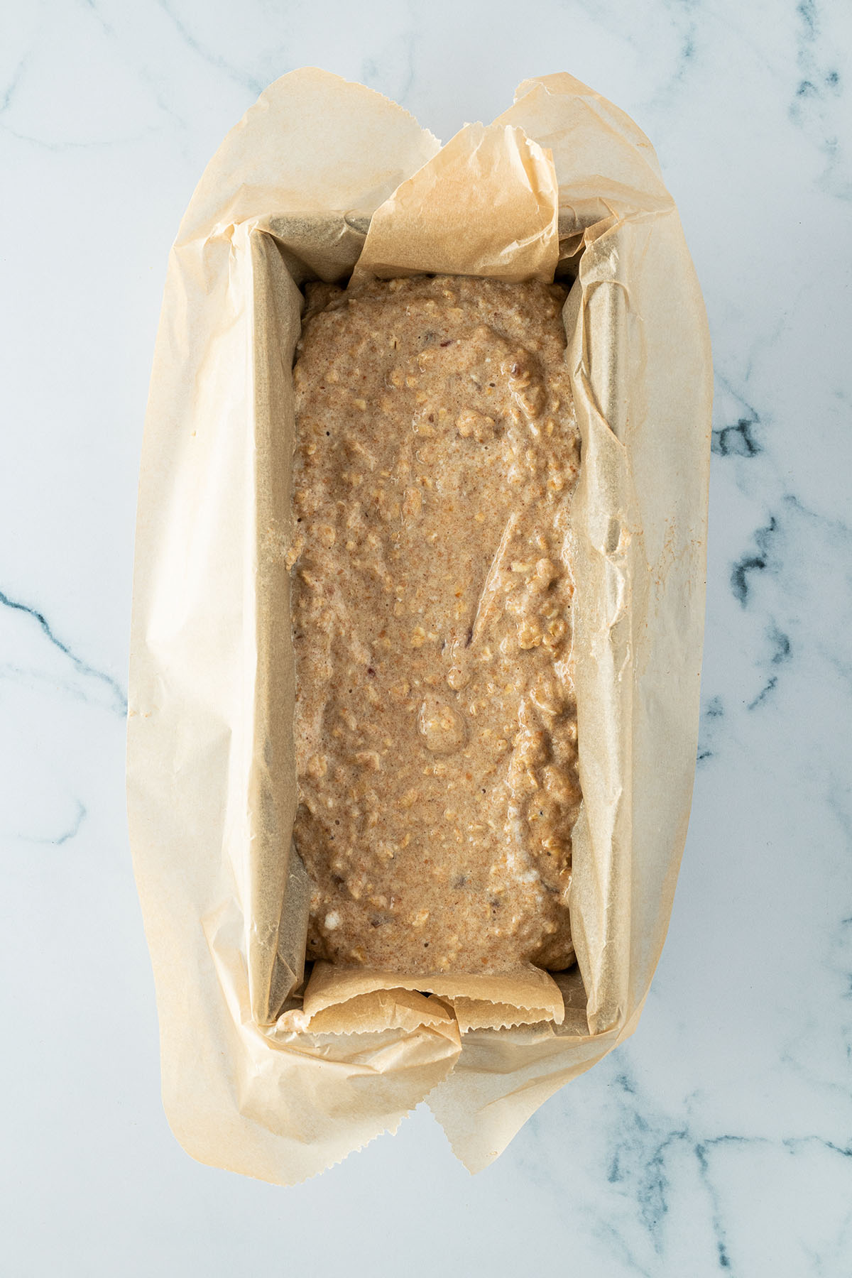 Bananenbrot Teig mit Haferflocken in eine mit Backpapier ausgekleidete Kastenform.