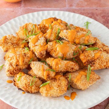Ein Teller mit panierten H&auml;hnchenst&uuml;cken auf roten Flie&szlig;en, serviert mit Bang Bang Chicken Sauce.