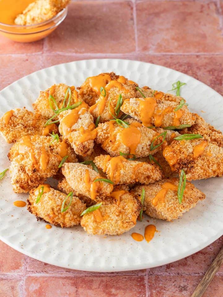 Ein Teller mit panierten H&auml;hnchenst&uuml;cken auf roten Flie&szlig;en, serviert mit Bang Bang Chicken Sauce.