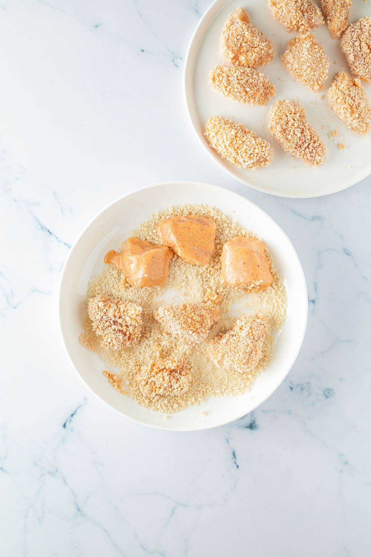 In Buttermilch marinierte H&auml;hnchenst&uuml;cke werden in einem Teller mit Panko paniert.