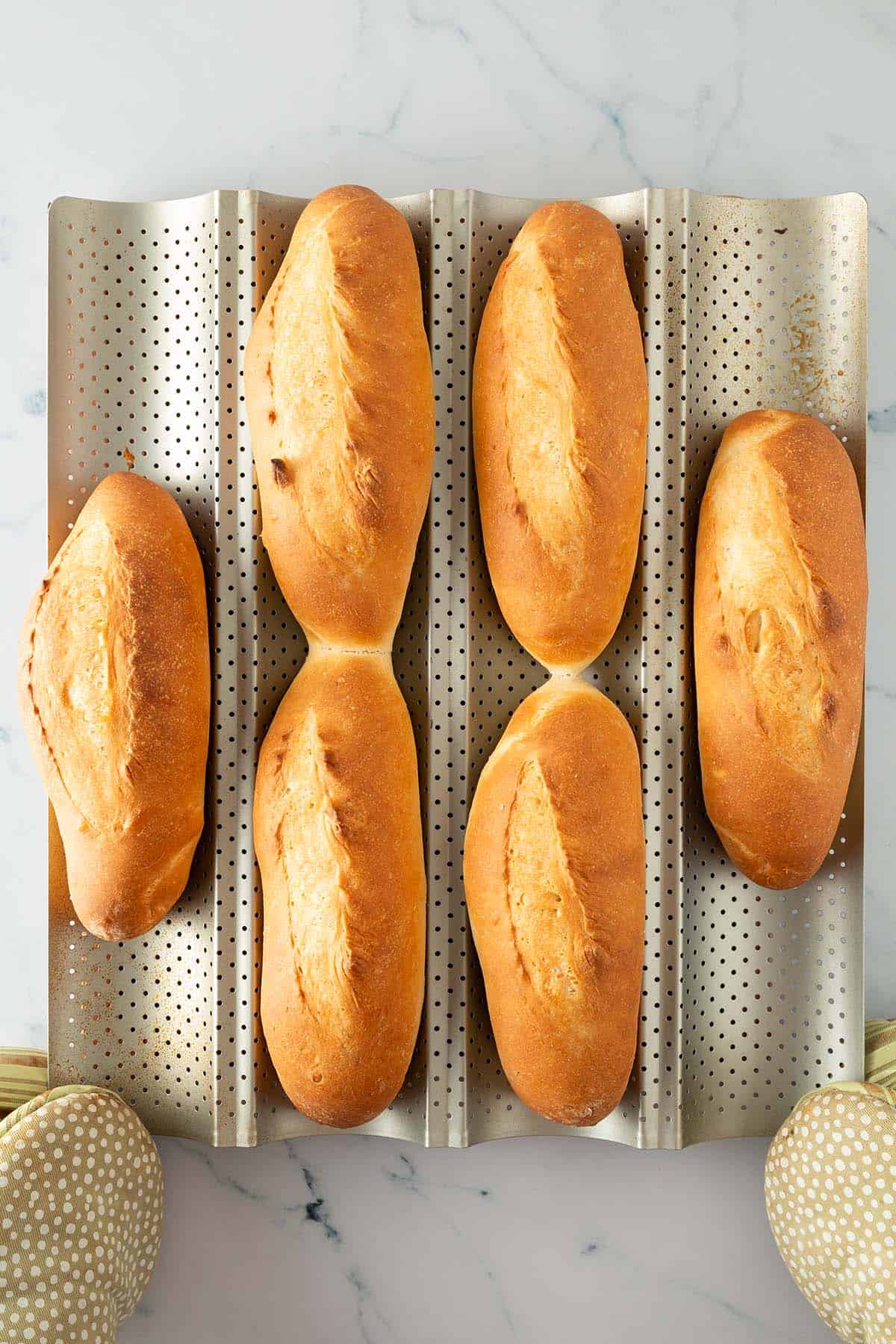 Sechs frisch gebackene Banh Mi Baguettes auf einem perforierten Baguetteblech, goldbraun und gleichm&auml;&szlig;ig gebacken.