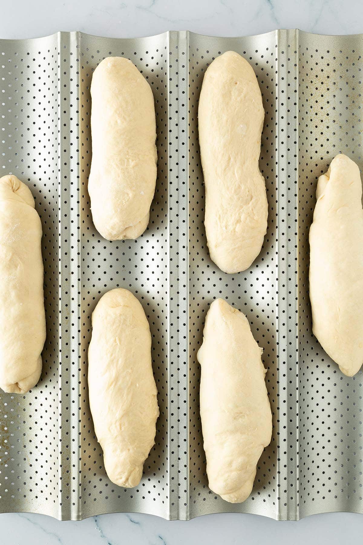 Sechs geformte Mini-Baguettes auf perforiertem Baguette-Backblech.