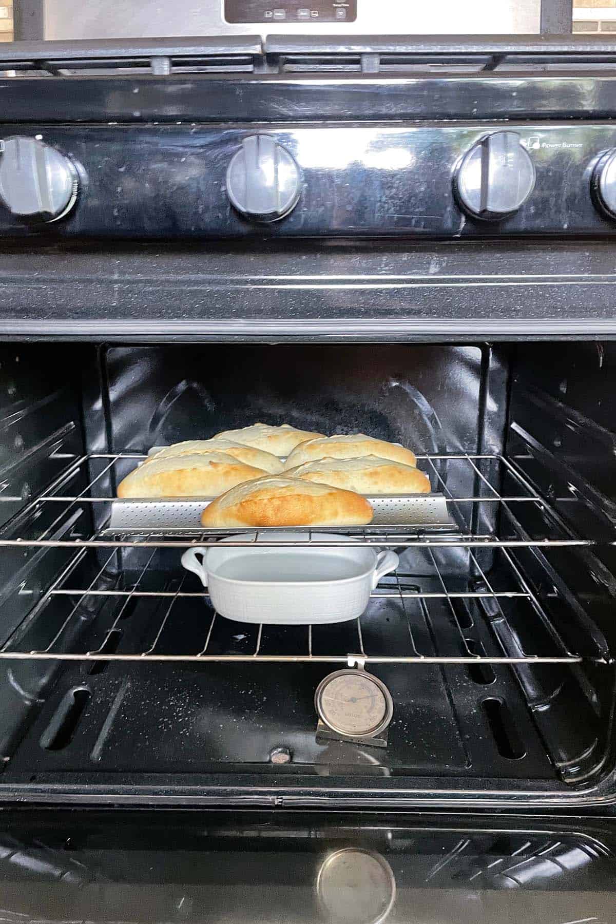 Baguette-Br&ouml;tchen backen im Ofen, mit einer Schale Wasser und Ofenthermometer auf dem Rost.