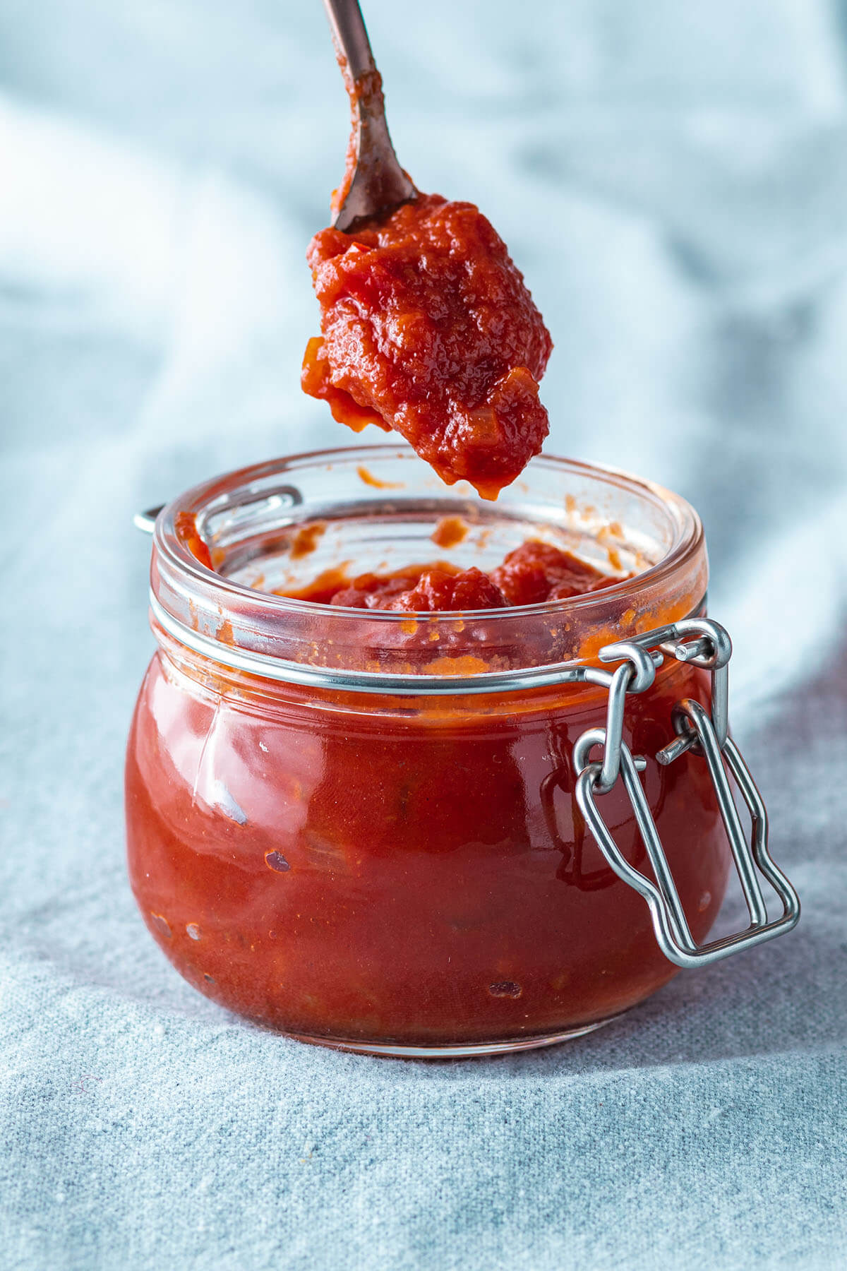 Ein L&ouml;ffel nimmt eine Portion selbstgemachte BBQ Sauce aus einem Gl&auml;schen.