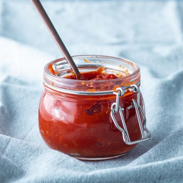 Selbstgemachte BBQ Sauce in einem kleinen Gl&auml;schen vor hellblauem Hintergrund.
