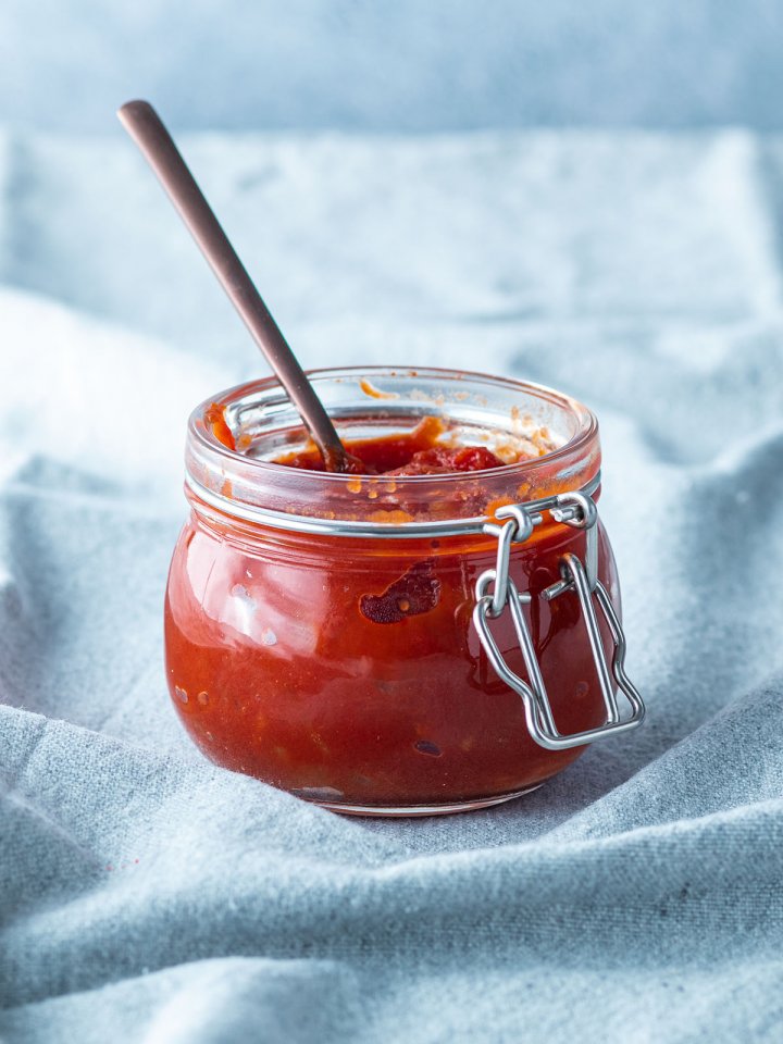 Selbstgemachte BBQ Sauce in einem kleinen Gl&auml;schen vor hellblauem Hintergrund.