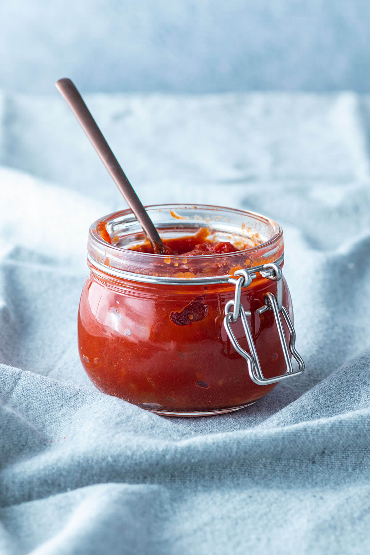 Selbstgemachte BBQ Sauce in einem kleinen Gl&auml;schen vor hellblauem Hintergrund.