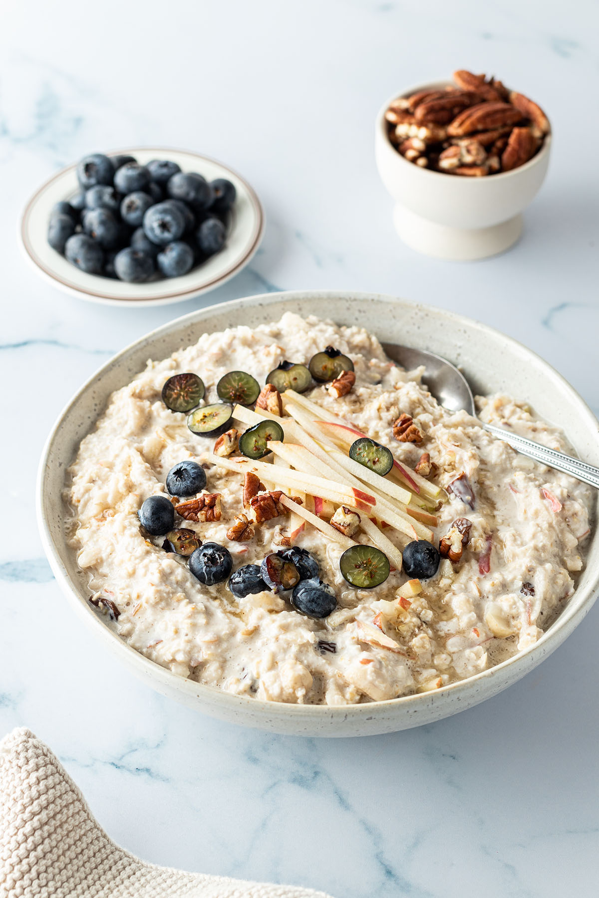 Bircher M&uuml;sli mit frischem Obst und N&uuml;ssen in einer Sch&uuml;ssel, frische Blaubeeren und N&uuml;sse im Hintergrund.