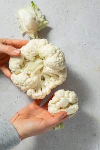 Blumenkohl wird mit den H&auml;nden in R&ouml;schen zerkleinert.