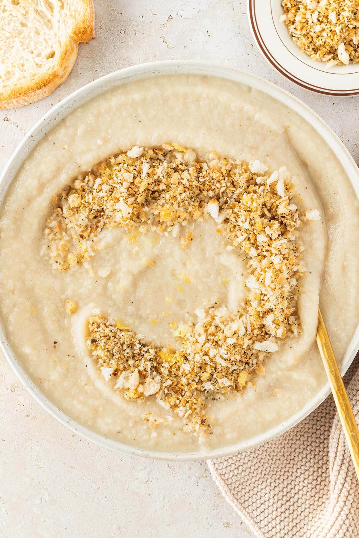 Vogelperspektive auf einen Teller Blumenkohlsuppe serviert mit einem knusprigen Brotkr&uuml;mel-Topping, Deko im Bildrand.