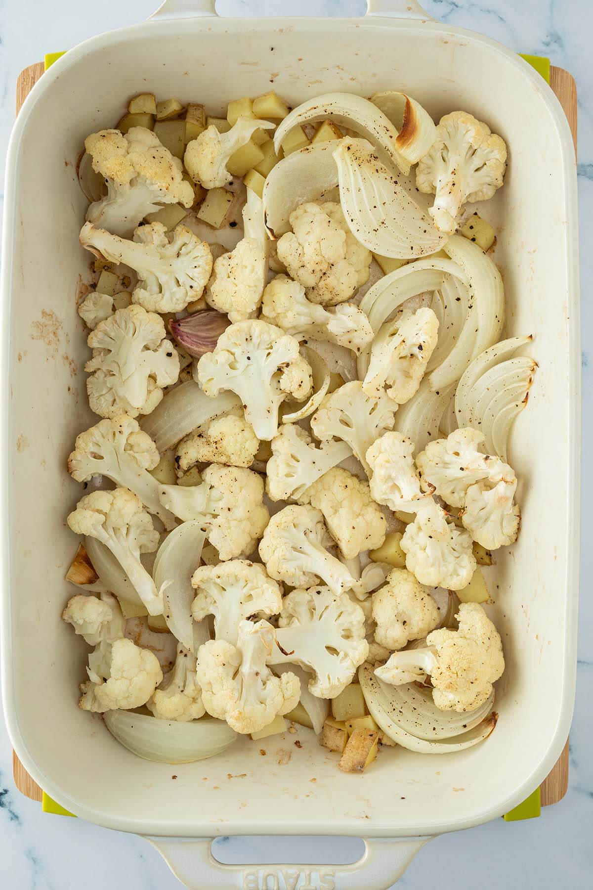 Auflaufform mit im Ofen ger&ouml;stetem Blumenkohl, Zwiebeln und kleinen Kartoffelw&uuml;rfeln.