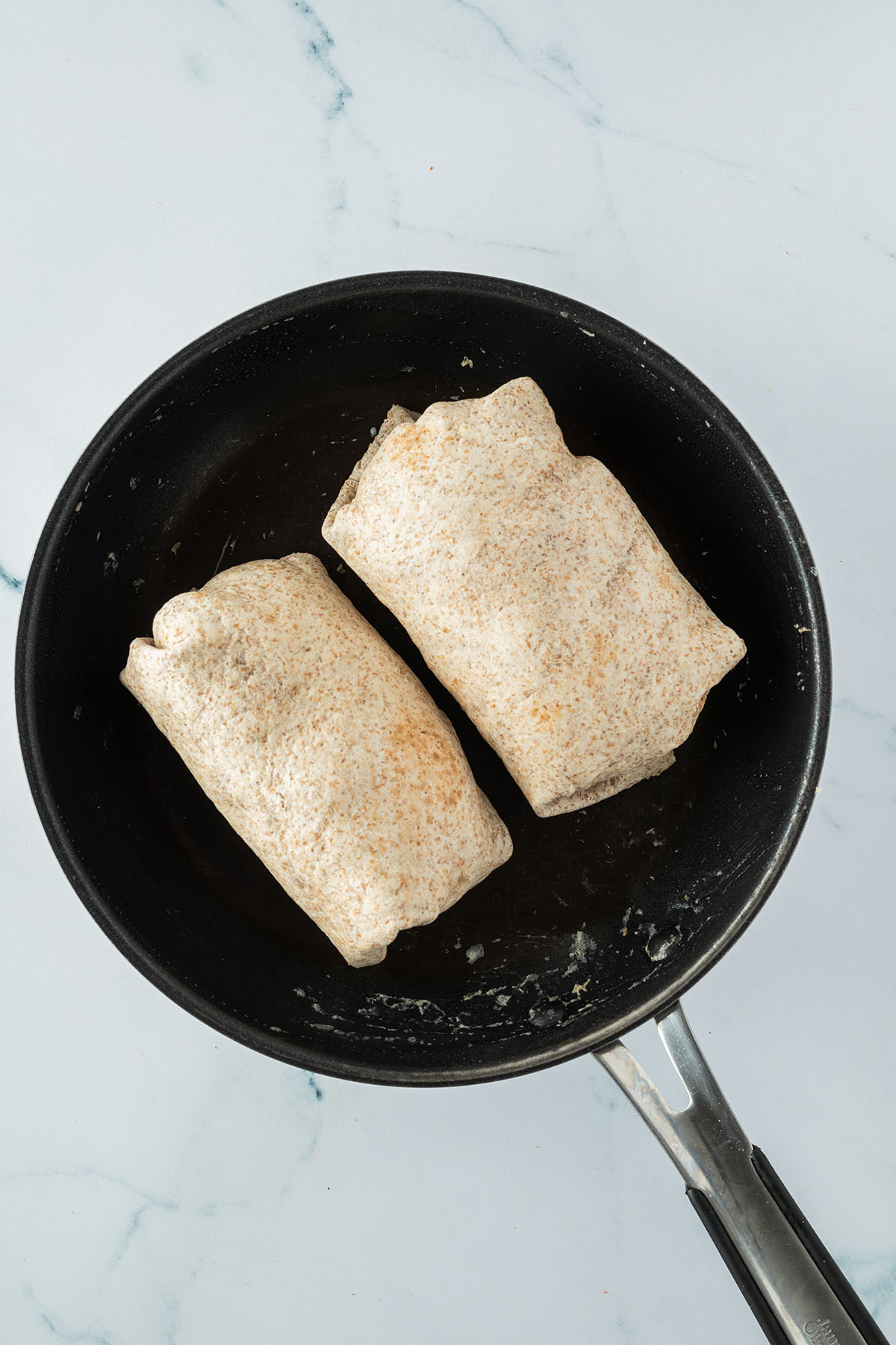 Zwei mit der Naht nach unten in der Pfanne liegende Burritos.