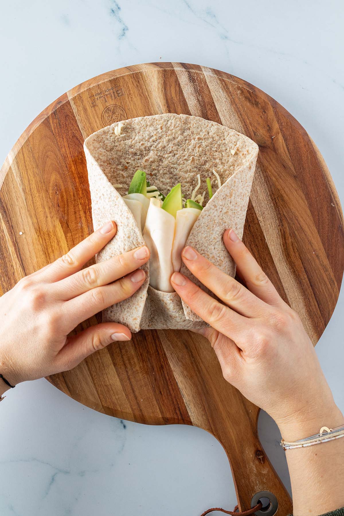 Ein Burrito, wo bereits die Unterseite sowie die beiden Seiten eingeschlagen wurden, wird von zwei H&auml;nden aufgerollt.