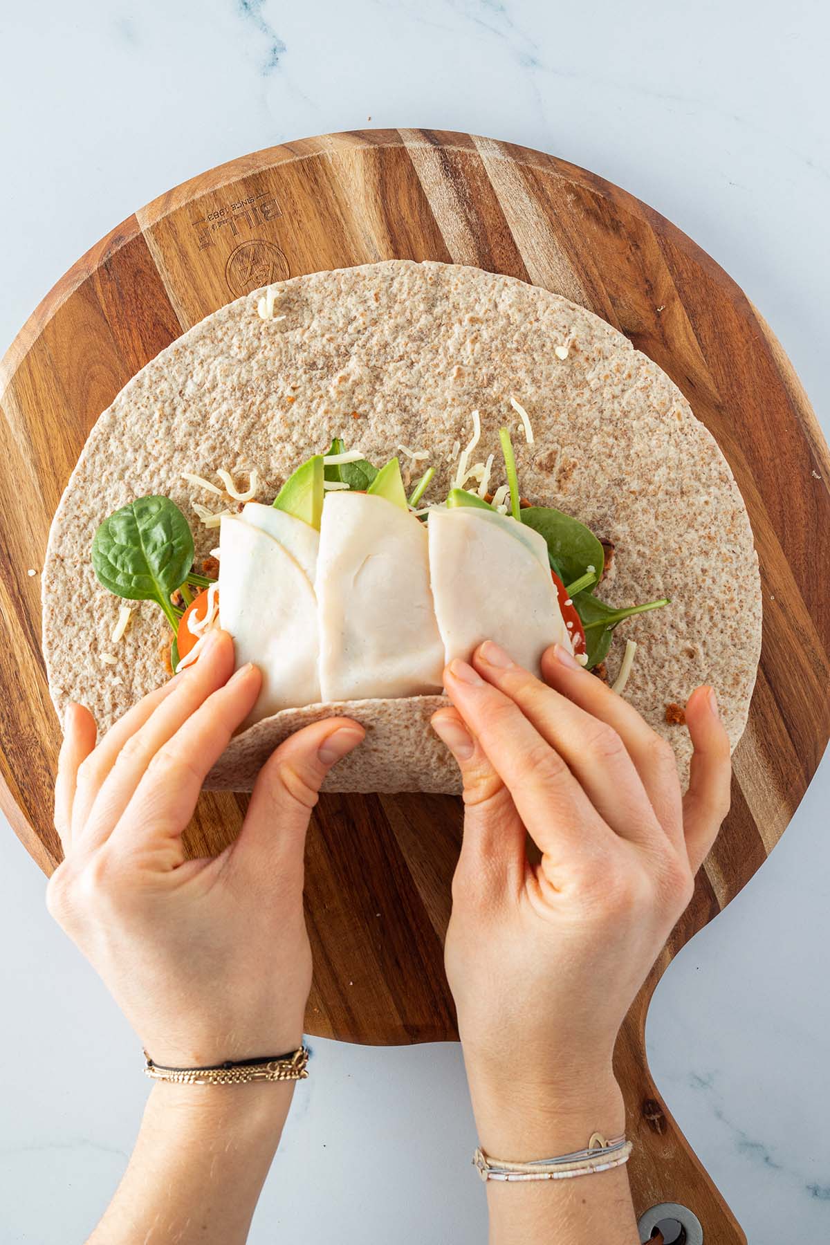 Die Unterseite eines, in der Mitte mit Zutaten belegten Weizenwraps, wird hochgeklappt.