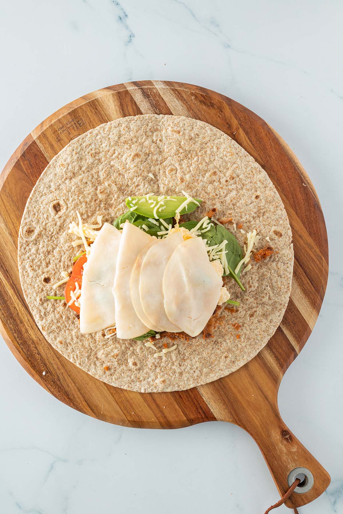 Ein belegter Weizentortilla auf einem runden Holzbrett.