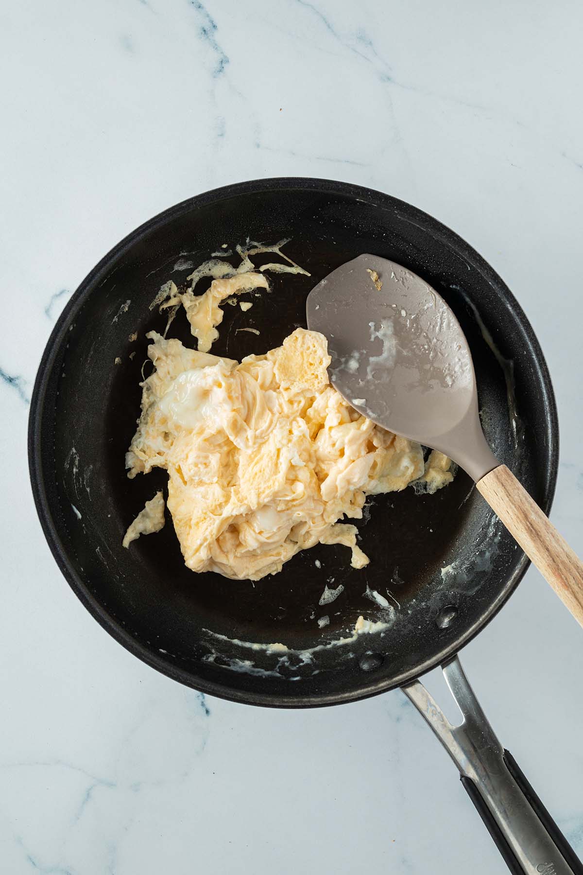 Eine Pfanne mit zwei Portionen R&uuml;hrei und einem Silikon-Pfannenwender daneben.