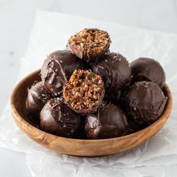 Mehrere ganze und halbierte, mit Schokolade &uuml;berzogene Brownie Energy Balls in einer kleinen Holzsch&uuml;ssel.