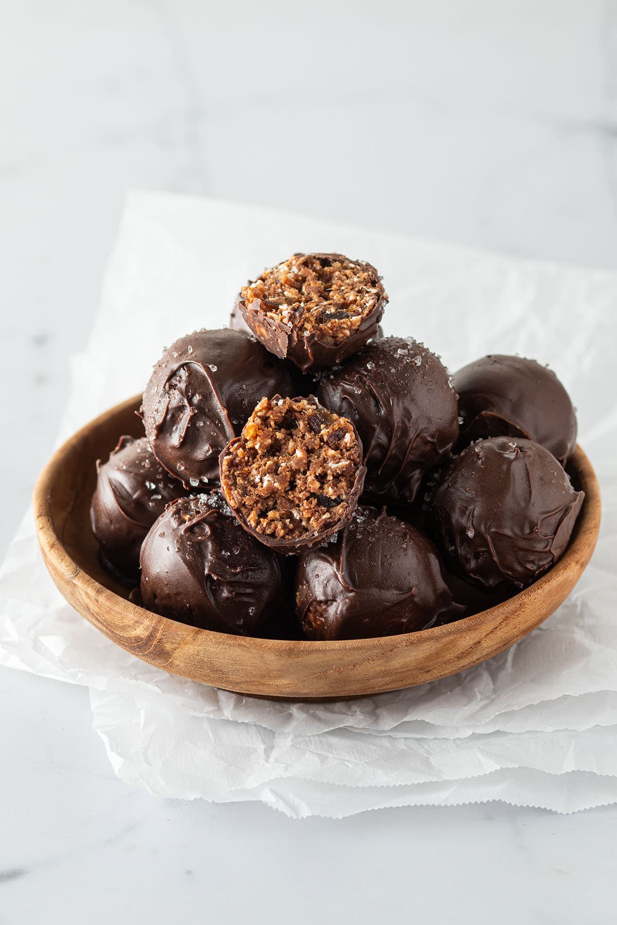 Mehrere ganze und halbierte, mit Schokolade &uuml;berzogene Brownie Energy Balls in einer kleinen Holzsch&uuml;ssel.