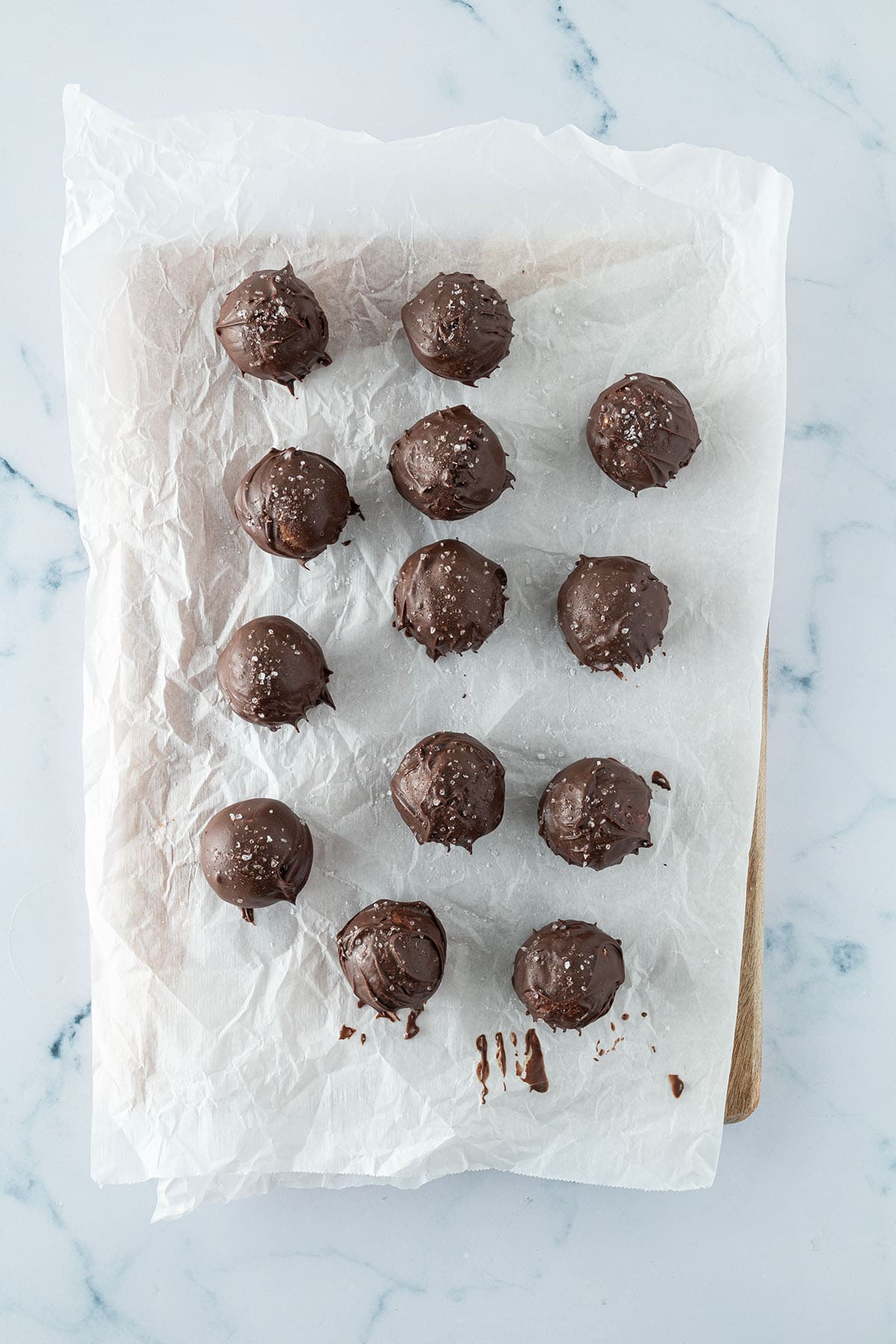 Mit Schokolade &uuml;berzogene Energy Balls auf einem St&uuml;ck Backpapier.