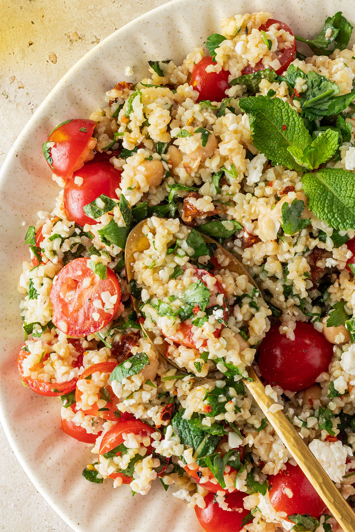 Nahaufnahme von einem Bulgur Salat mit Tomaten, Petersilie, Minze, Kichererbsen und Feta.