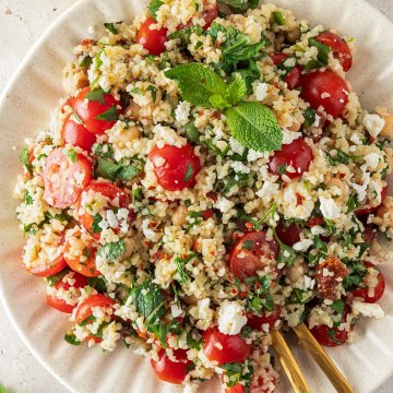 Bulgur Salat mit Feta und frischem Gem&uuml;se auf einem wei&szlig;en Teller auf einem Steinuntergrund.