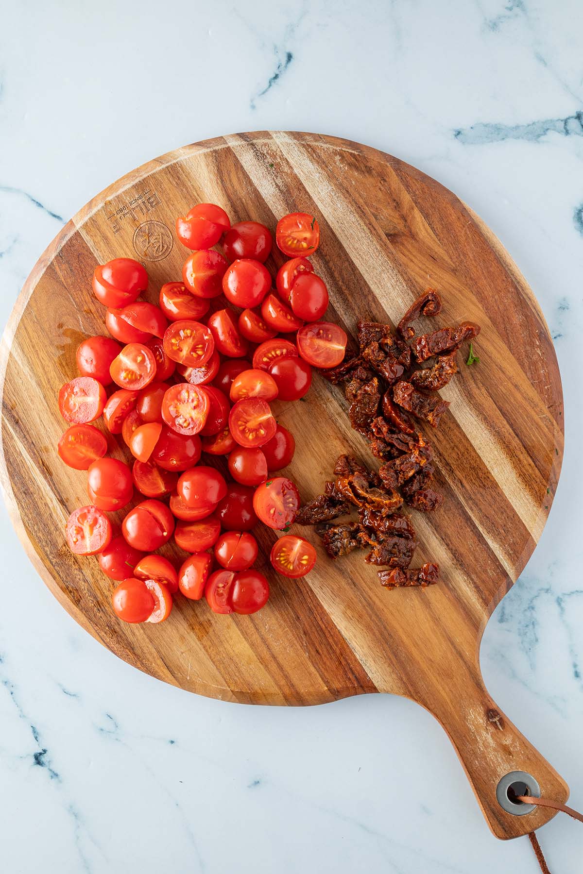 Halbierte Kirschtomaten und in d&uuml;nne Streifen geschnittene getrocknete Tomaten auf einem Holzbrett.