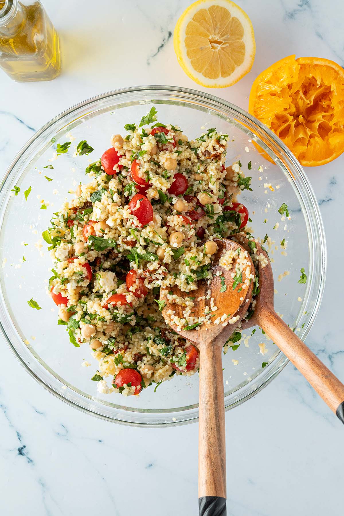 Bulgursalat in einer gro&szlig;en Sch&uuml;ssel mit Salatbesteck, daneben eine ausgepresste Orange, eine halbe Zitrone und eine Flasche Oliven&ouml;l.