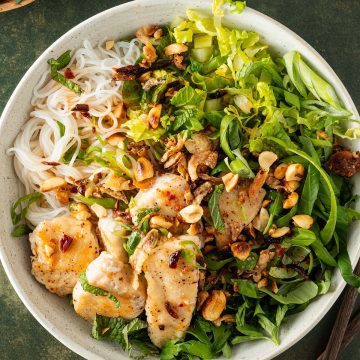 Eine Sch&uuml;ssel Bun Tron, ein vietnamesischer Reisnudelsalat mit frischen Kr&auml;utern, Salat, H&auml;hnchen und knusprigen Erdn&uuml;ssen, auf einem dunkelgr&uuml;nen Untergrund.