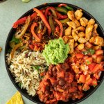 Selbstgemachte Burrito Bowl in einem tiefen Teller mit verscheidenen Komponenten, die nebeneinander angeordnet sind. Daneben eine Sch&uuml;ssel mit Salsa, eine Limetten-Spalte und Nachos.