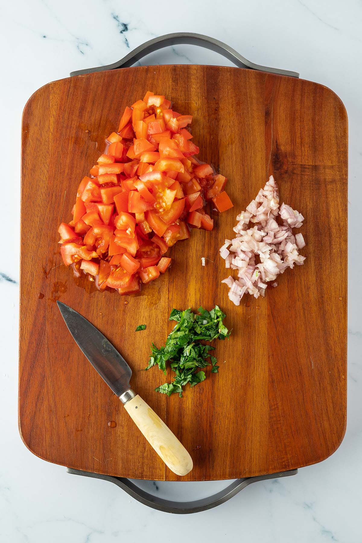 Kleingew&uuml;rfelte Tomaten, Zwiebeln und gehackter Koriander auf einem Holzbrett.