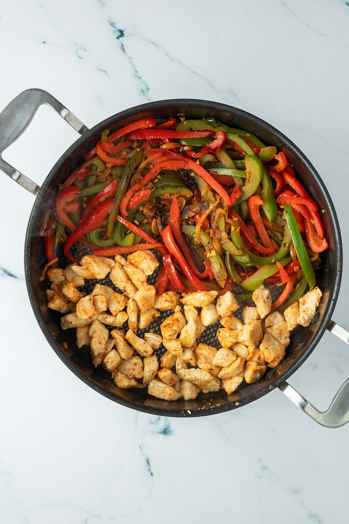 Gro&szlig;e Sautierpfanne mit Fajitas-Gem&uuml;se auf einer und angebratenen H&auml;hnchenst&uuml;cke auf der anderen Seite.