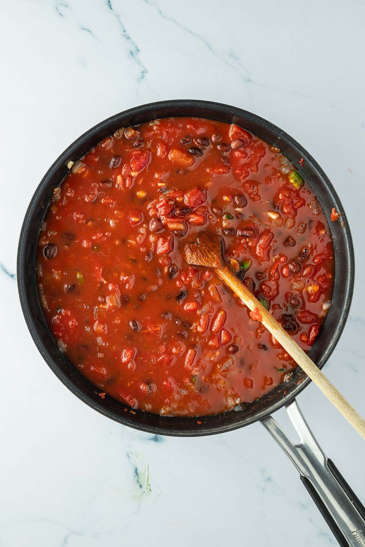 Vogelperspektive auf eine Pfanne mit einer noch sehr fl&uuml;ssigen Tomaten-Bohnen-Mischung.