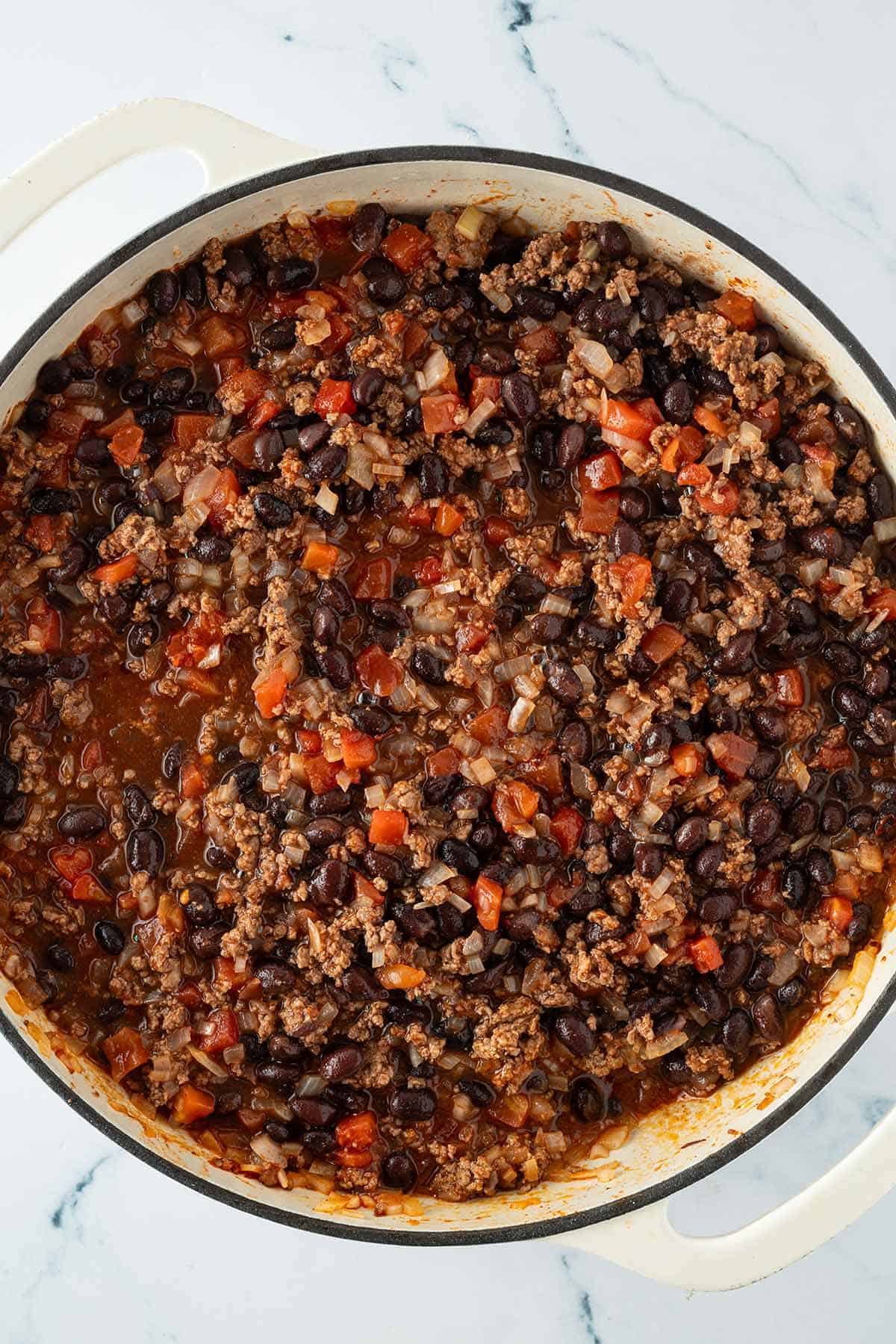 In einer gro&szlig;en Pfanne kochen angebratenes Hackfleisch und schwarze Bohnen in Tomatensauce.