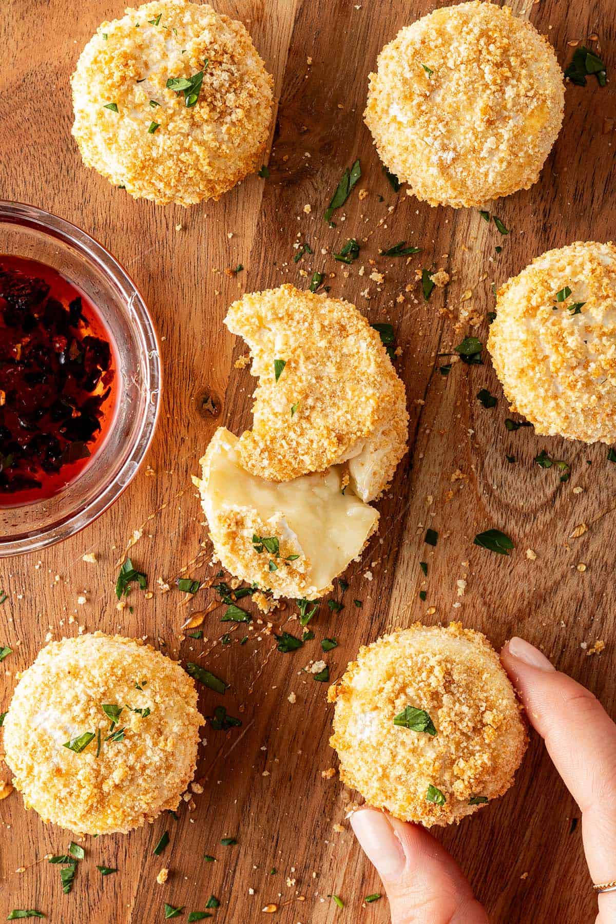 Gebackene Camemberts aus dem Airfryer mit knuspriger Panade auf einem Holzbrett mit Petersilie und Dip.