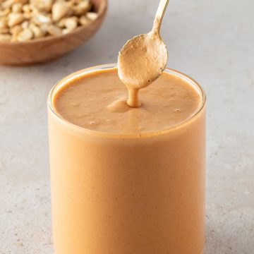 Cremiges Cashew-Dressing in einem Glas, mit einem L&ouml;ffel und Cashews im Hintergrund.