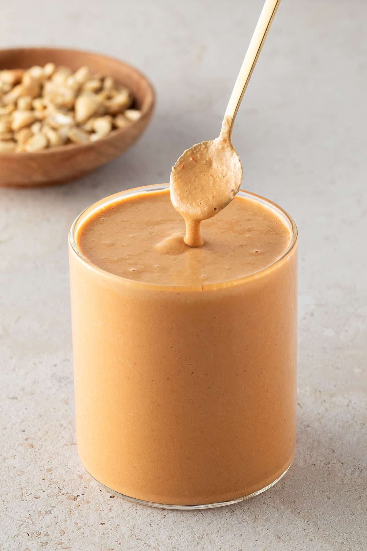 Cremiges Cashew-Dressing in einem Glas, mit einem L&ouml;ffel und Cashews im Hintergrund.