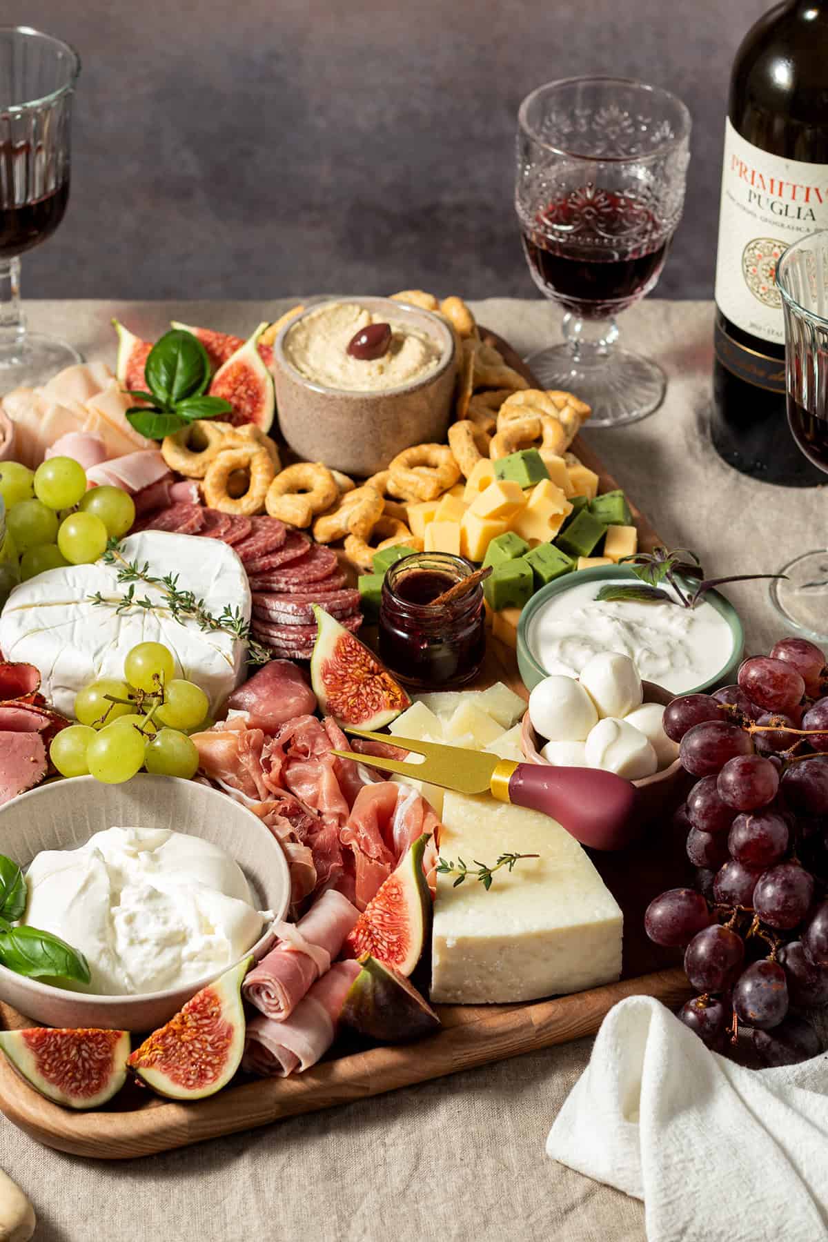 Gro&szlig;e Charcuterie-Platte mit K&auml;se, Wurst, Trauben, Feigen, Dips und Crackern, angerichtet auf einem Holzbrett, daneben Rotwein.