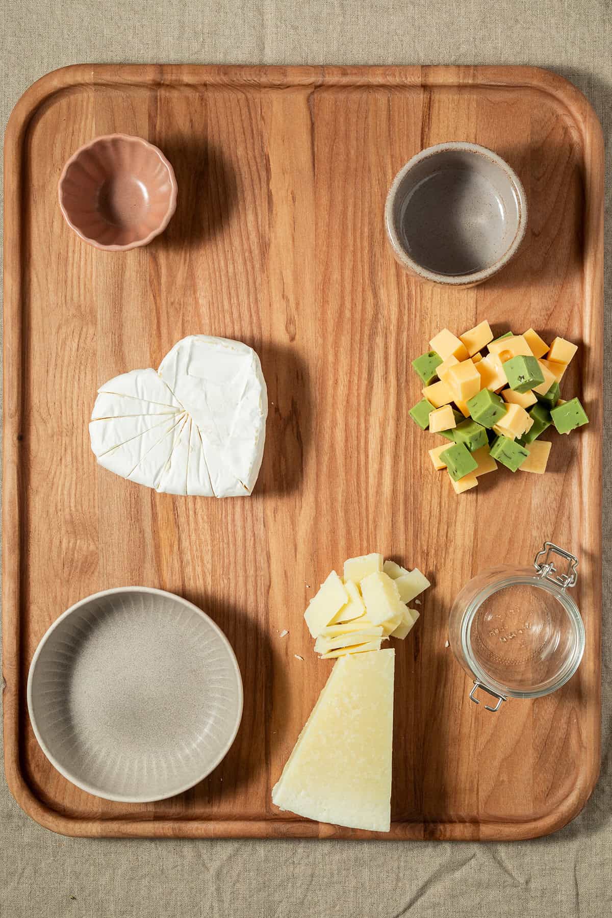 Leeres Holzbrett mit vorbereiteten Sch&auml;lchen und verschiedenen K&auml;sesorten als Grundlage zum Anrichten einer Charcuterie-Platte.