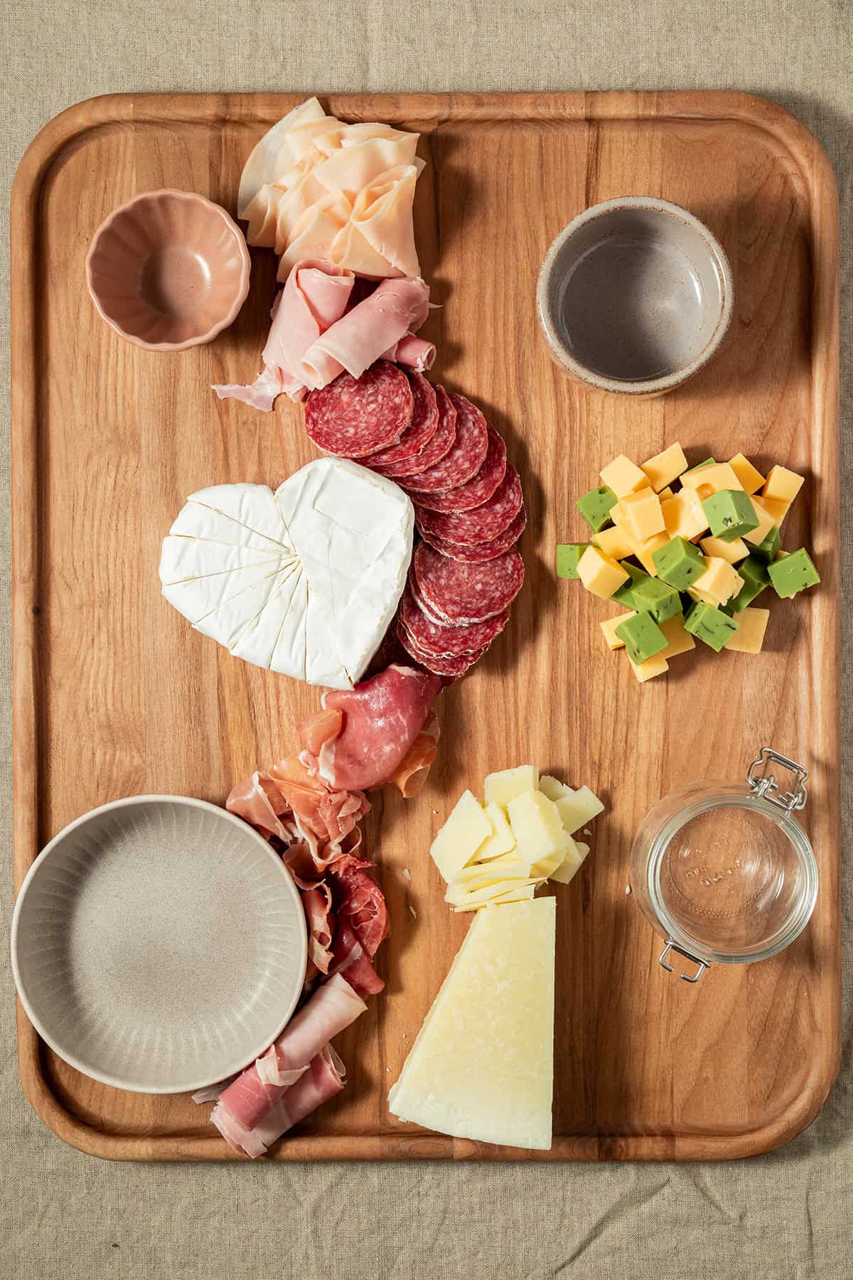 Holzbrett mit angeordneten Wurst- und K&auml;sesorten sowie leeren Sch&auml;lchen.
