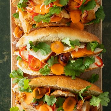 Drei Chicken Banh Mi Sandwiches mit eingelegten Karotten, Chili und frischem Koriander auf Holzbrett.