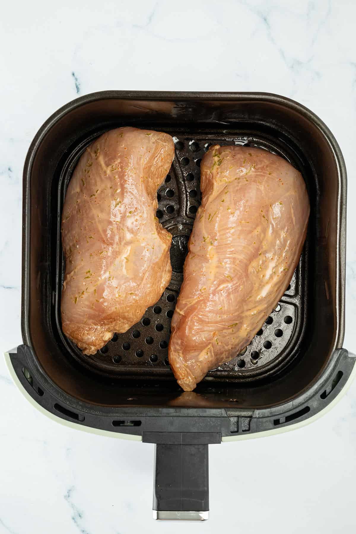 Zwei marinierte H&auml;hnchenbrustfilets im Airfryer-Korb vor dem Garen.