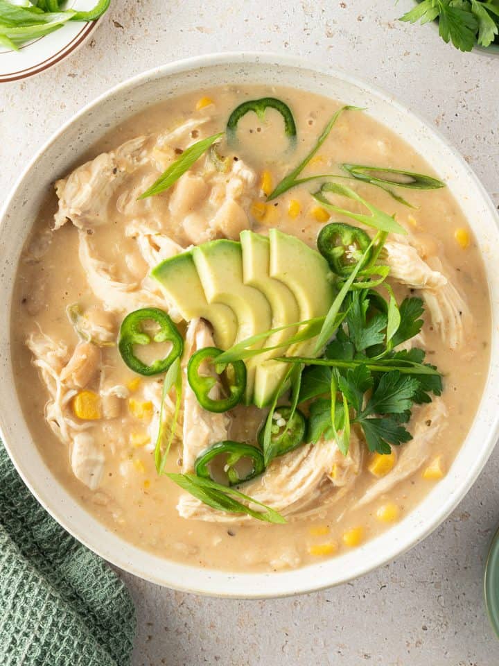 Eine Sch&uuml;ssel mit cremigen H&auml;hnchen Curry mit wei&szlig;en Bohnen, Mais, Avocado und frischen Kr&auml;utern.