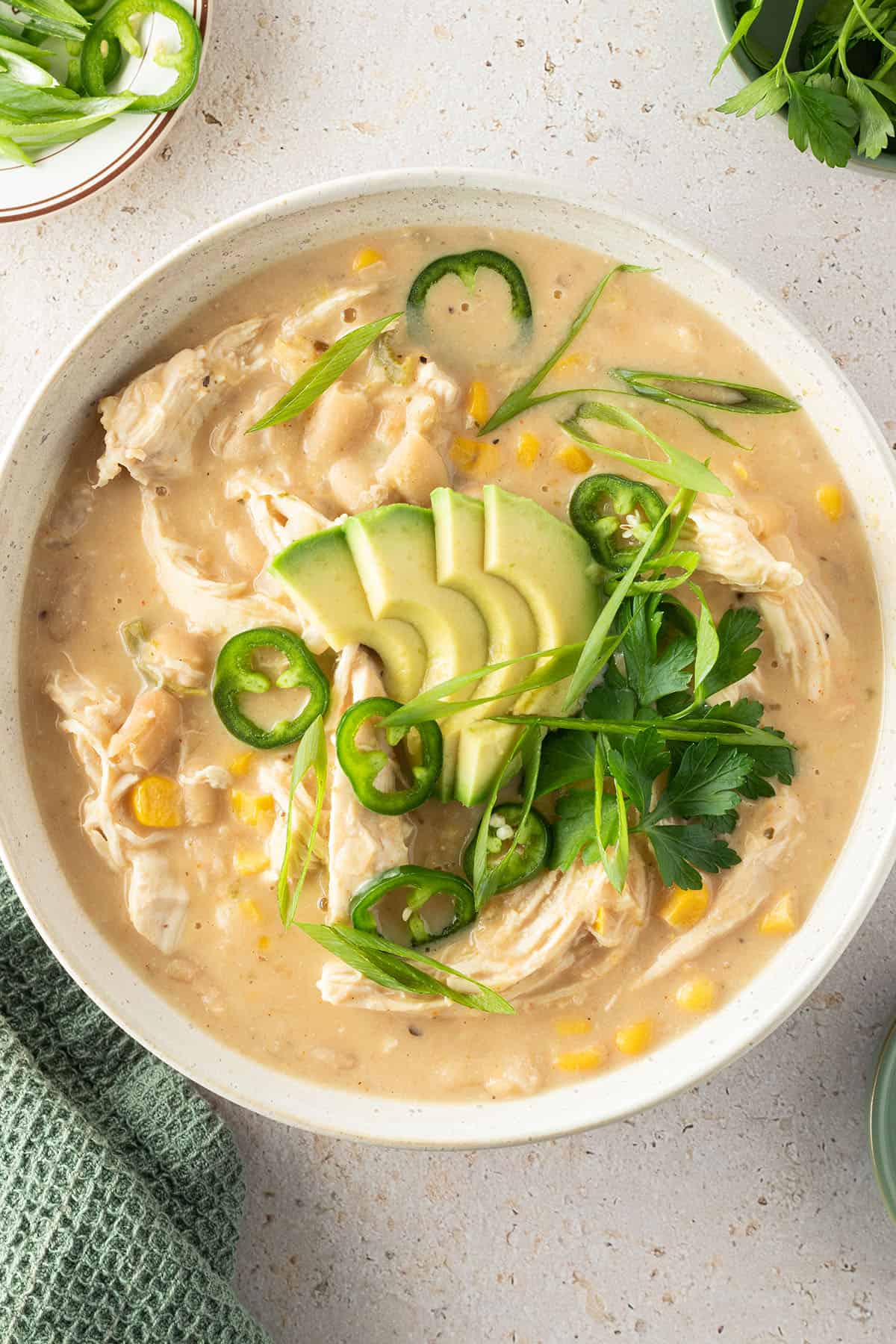Eine Sch&uuml;ssel mit cremigen H&auml;hnchen Curry mit wei&szlig;en Bohnen, Mais, Avocado und frischen Kr&auml;utern.